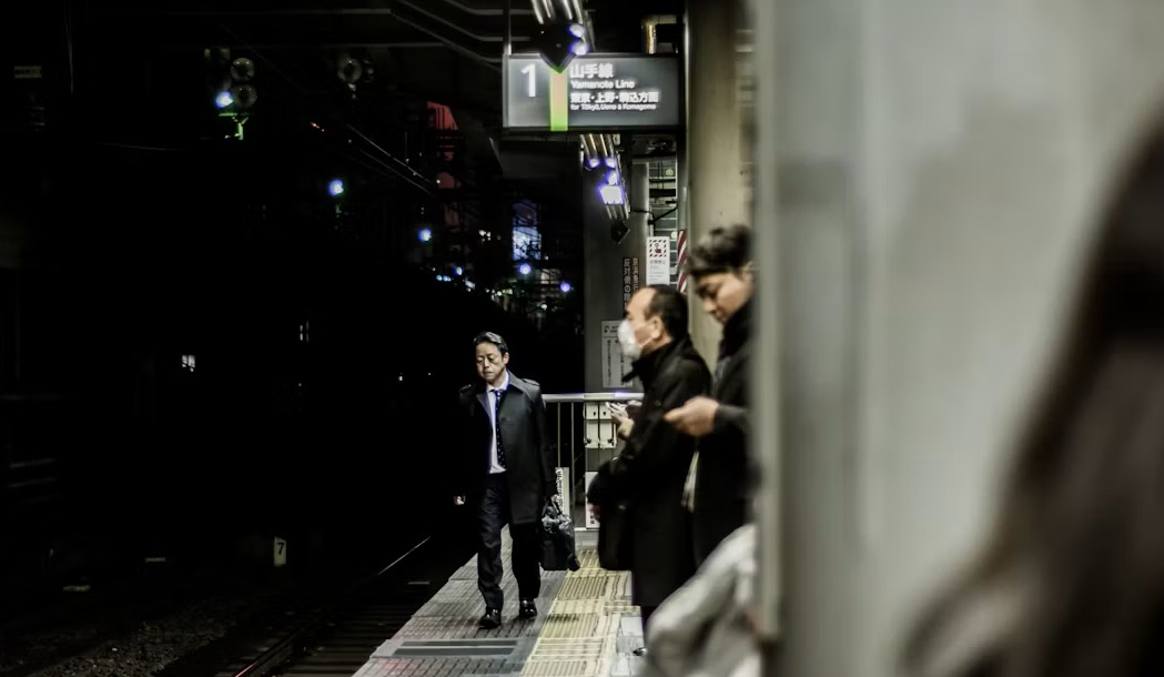夜の駅のホームで電車を待つ通勤客のようす
